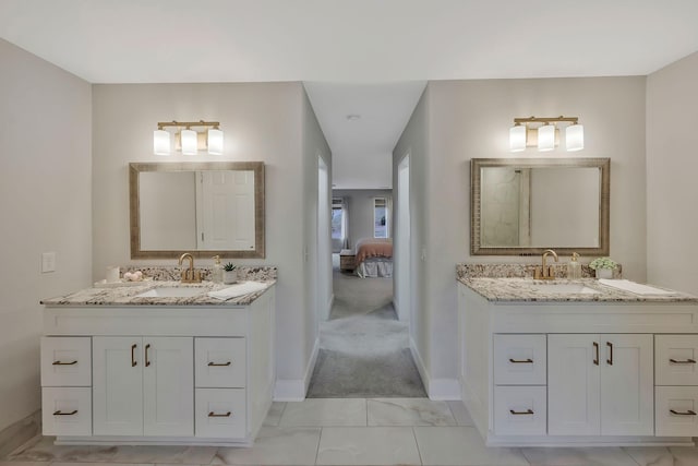 ensuite bathroom featuring two vanities, baseboards, and a sink