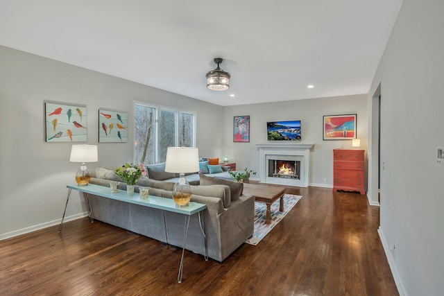 living room featuring recessed lighting, baseboards, dark wood-style flooring, and a lit fireplace