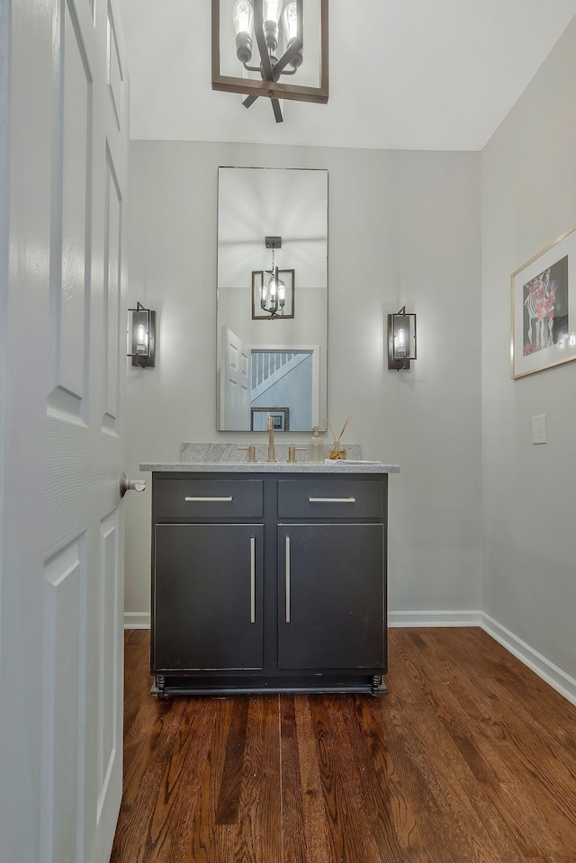 bar with dark wood finished floors, a sink, baseboards, and a chandelier