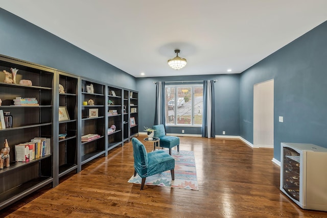 sitting room featuring wood finished floors, a notable chandelier, beverage cooler, and baseboards