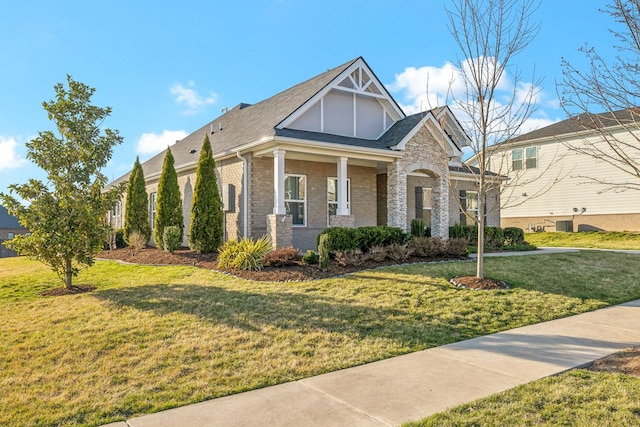 view of front facade with stone siding, brick siding, a front yard, and a shingled roof