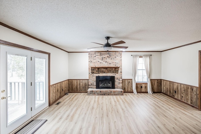 unfurnished living room featuring wooden walls, a brick fireplace, a wainscoted wall, light wood-type flooring, and a textured ceiling