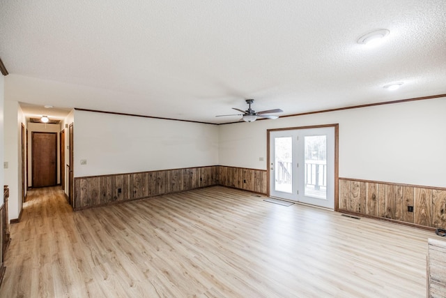 empty room with wainscoting, a textured ceiling, and wood walls