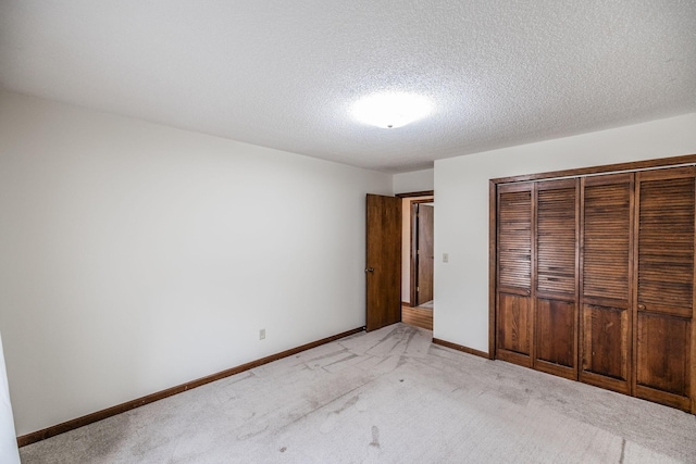 unfurnished bedroom featuring a closet, light colored carpet, a textured ceiling, and baseboards