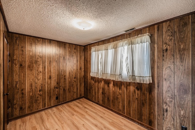 empty room with visible vents, baseboards, wood walls, light wood-type flooring, and a textured ceiling