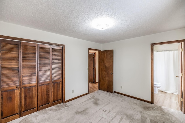 unfurnished bedroom featuring baseboards, a closet, a textured ceiling, light colored carpet, and connected bathroom