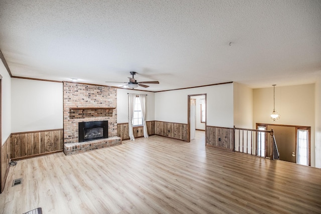 unfurnished living room featuring a textured ceiling, a brick fireplace, wooden walls, and wainscoting