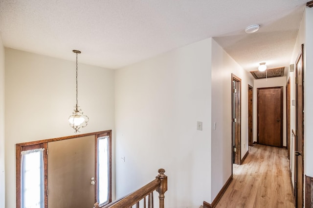 hallway with visible vents, a textured ceiling, light wood-style floors, baseboards, and attic access