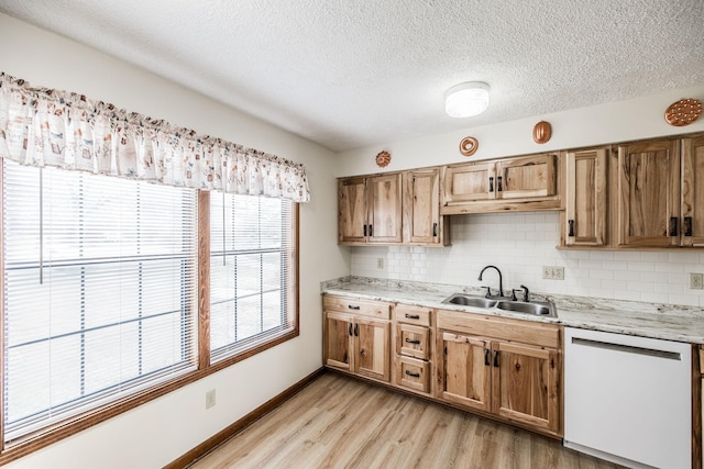 kitchen with baseboards, dishwasher, decorative backsplash, light wood-style flooring, and a sink