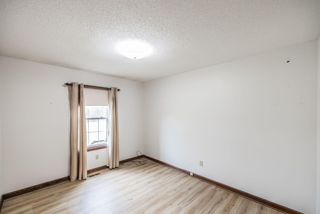 empty room featuring light wood-style flooring, visible vents, baseboards, and a textured ceiling