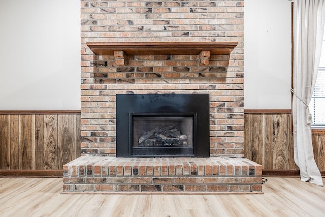 details featuring wainscoting, a brick fireplace, wood walls, and wood finished floors