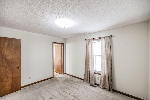 spare room featuring visible vents, baseboards, a textured ceiling, and light carpet