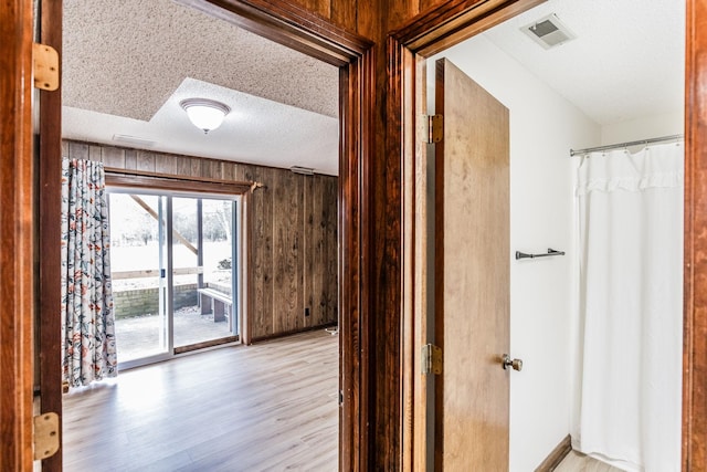 corridor with visible vents, a textured ceiling, wood walls, light wood finished floors, and baseboards