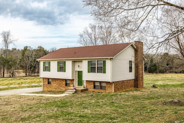 raised ranch with driveway, a front lawn, fence, a shingled roof, and a chimney