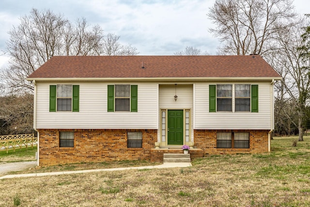 raised ranch featuring brick siding, a front lawn, fence, entry steps, and roof with shingles