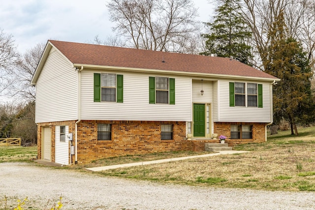 raised ranch with brick siding, a shingled roof, gravel driveway, and a garage