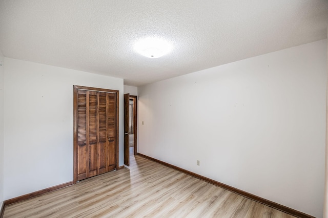 empty room featuring baseboards, light wood-type flooring, and a textured ceiling