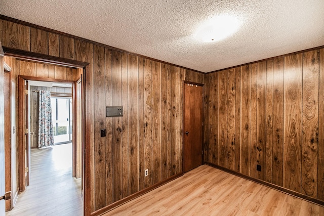 empty room featuring a textured ceiling, wood walls, and light wood finished floors