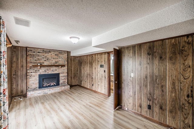 unfurnished living room featuring visible vents, a brick fireplace, wooden walls, and wood finished floors