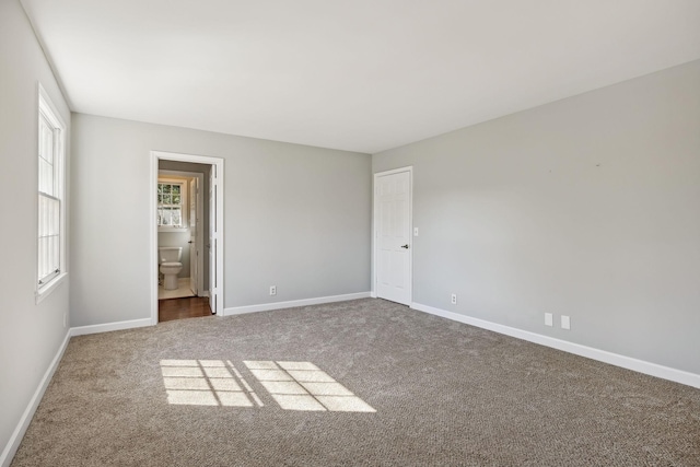 unfurnished bedroom with baseboards, ensuite bathroom, and carpet flooring