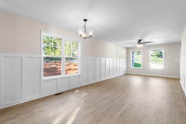 spare room with visible vents, light wood-type flooring, wainscoting, ceiling fan with notable chandelier, and a decorative wall