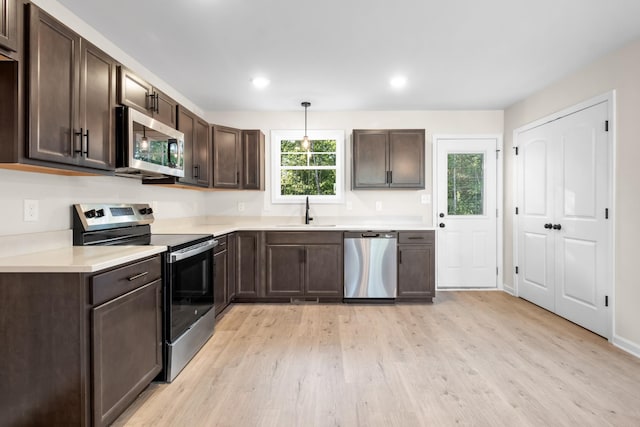 kitchen featuring light wood finished floors, a sink, stainless steel appliances, light countertops, and dark brown cabinets