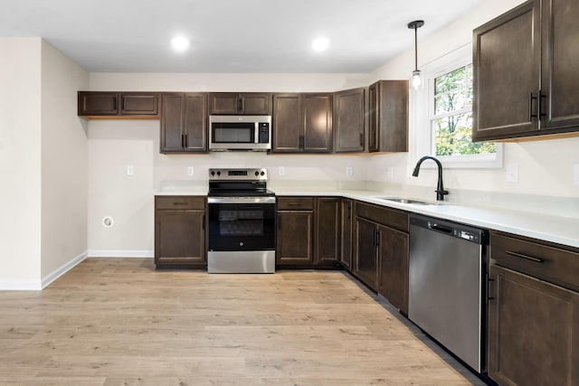 kitchen featuring dark brown cabinets, appliances with stainless steel finishes, light wood-style floors, and a sink