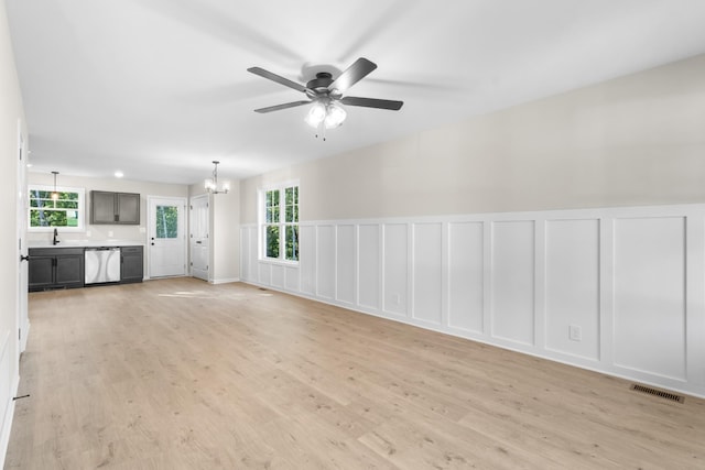 unfurnished living room featuring a decorative wall, a healthy amount of sunlight, visible vents, and light wood finished floors