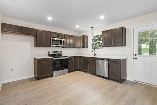 kitchen featuring light wood-style flooring, a sink, dark brown cabinetry, appliances with stainless steel finishes, and light countertops