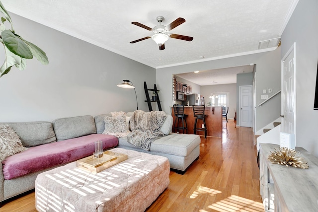 living area featuring visible vents, ceiling fan, crown molding, and light wood finished floors