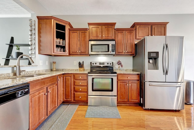 kitchen with light stone counters, light wood finished floors, a sink, stainless steel appliances, and brown cabinets