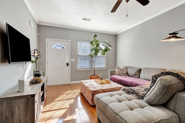 living room featuring light wood finished floors, baseboards, ornamental molding, a textured ceiling, and a ceiling fan