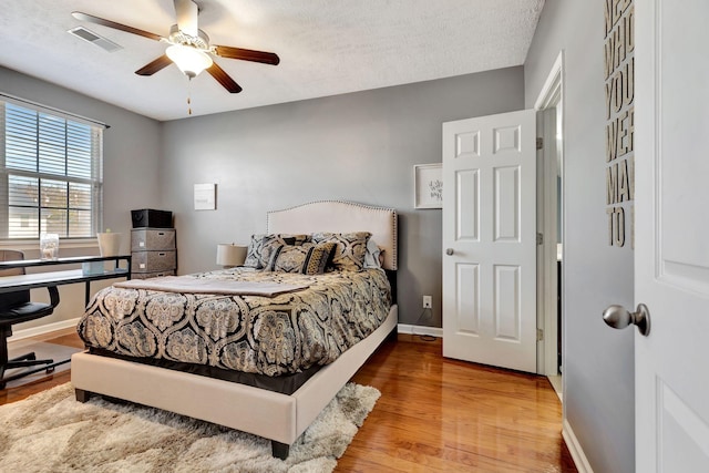 bedroom with wood finished floors, baseboards, visible vents, ceiling fan, and a textured ceiling