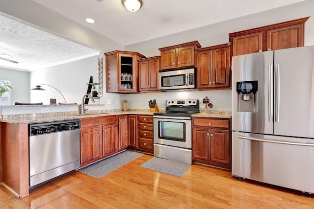 kitchen featuring light wood finished floors, a peninsula, brown cabinetry, stainless steel appliances, and a sink