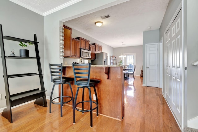 kitchen featuring visible vents, a kitchen breakfast bar, stainless steel appliances, brown cabinetry, and light wood finished floors