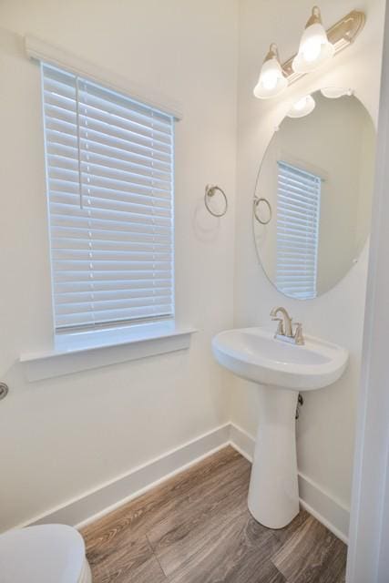 half bathroom featuring toilet, wood finished floors, baseboards, and a sink