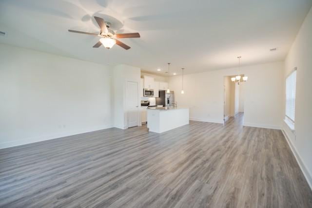 unfurnished living room with visible vents, baseboards, wood finished floors, and ceiling fan with notable chandelier