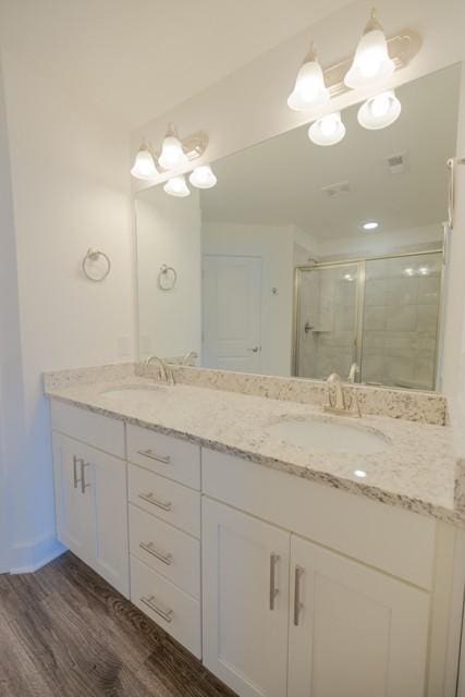 full bathroom featuring a sink, double vanity, wood finished floors, and a shower stall