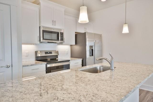 kitchen with a sink, light stone counters, backsplash, white cabinetry, and stainless steel appliances