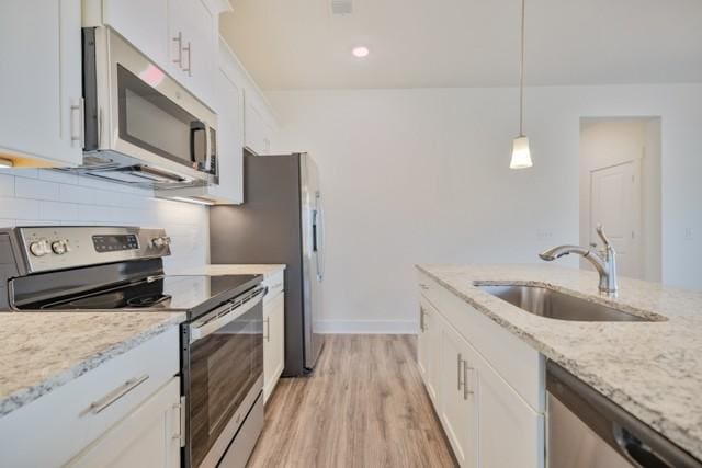 kitchen featuring tasteful backsplash, light stone counters, white cabinets, stainless steel appliances, and a sink