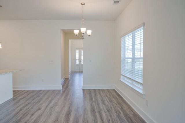 unfurnished dining area featuring visible vents, baseboards, an inviting chandelier, and wood finished floors