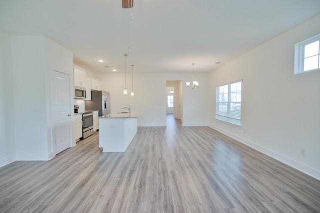 kitchen featuring stainless steel appliances, open floor plan, white cabinets, and light wood-style flooring