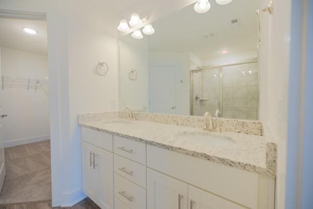 full bathroom with a shower stall, a spacious closet, double vanity, and a sink