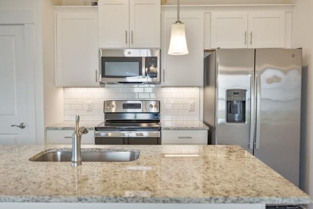 kitchen with light stone counters, a sink, stainless steel appliances, white cabinets, and backsplash