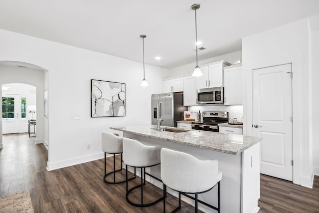 kitchen with dark wood-type flooring, decorative backsplash, appliances with stainless steel finishes, arched walkways, and a sink