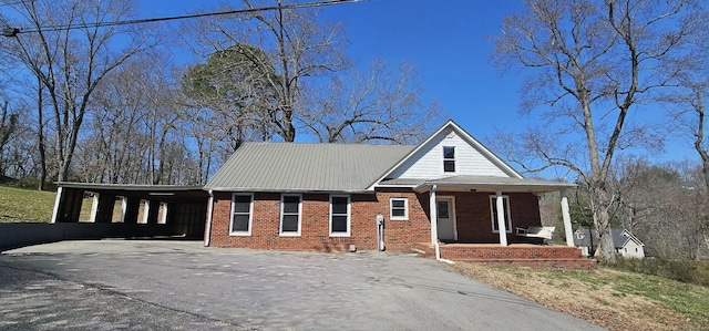 view of front facade featuring brick siding, covered porch, driveway, and a carport