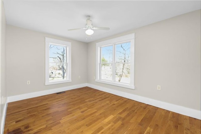 spare room featuring visible vents, a ceiling fan, baseboards, and wood finished floors