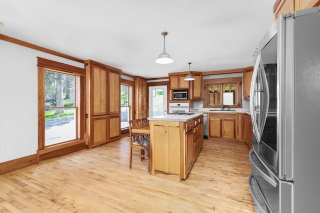kitchen with light wood finished floors, a center island, light countertops, appliances with stainless steel finishes, and brown cabinetry