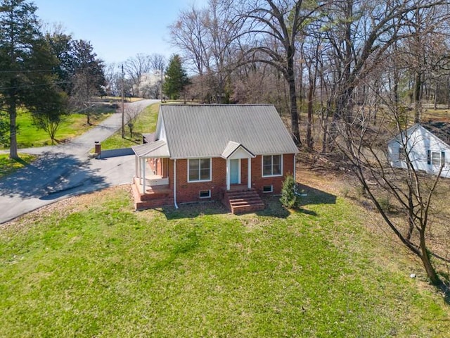 view of front of property featuring metal roof, a front yard, brick siding, and driveway