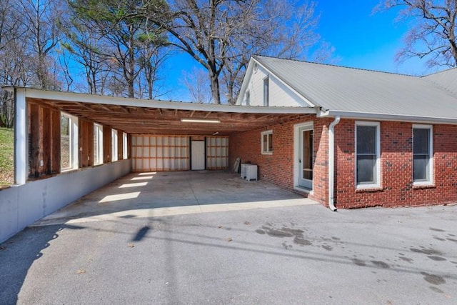 view of side of property featuring a carport, driveway, metal roof, and brick siding